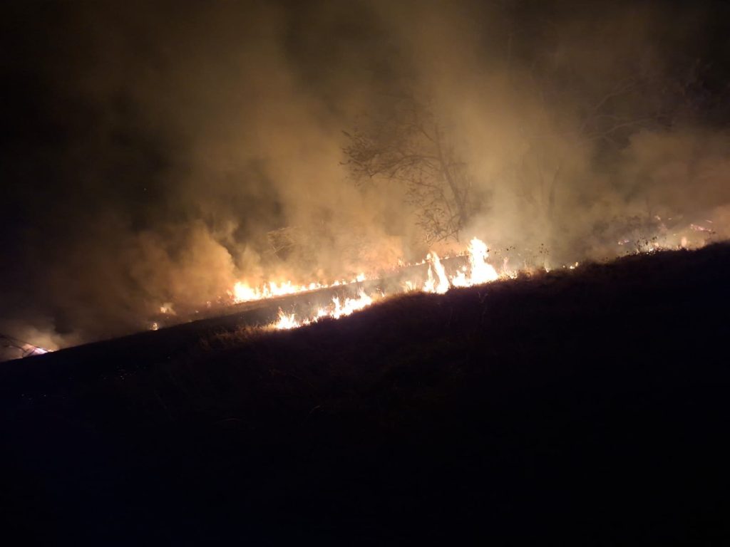Llamas y humo se extienden sobre una ladera durante la noche.