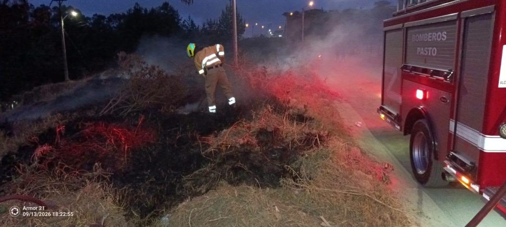 Atención del incendio al anochecer, con personal bomberil y un vehículo de emergencia junto al área afectada.